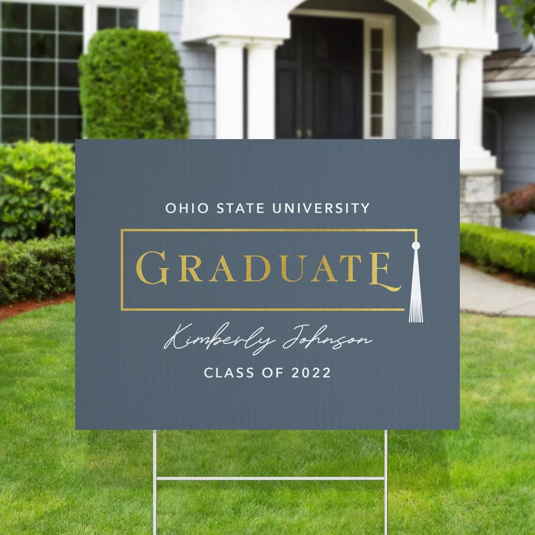 Ohio State University graduate yard sign with gold text on gray background in a front yard