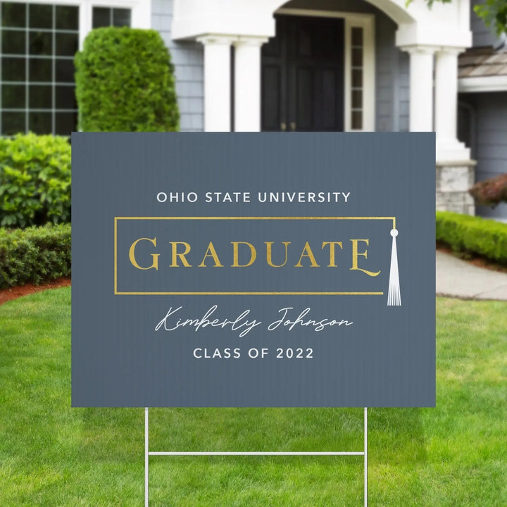 Ohio State University graduate yard sign with gold text on gray background in a front yard