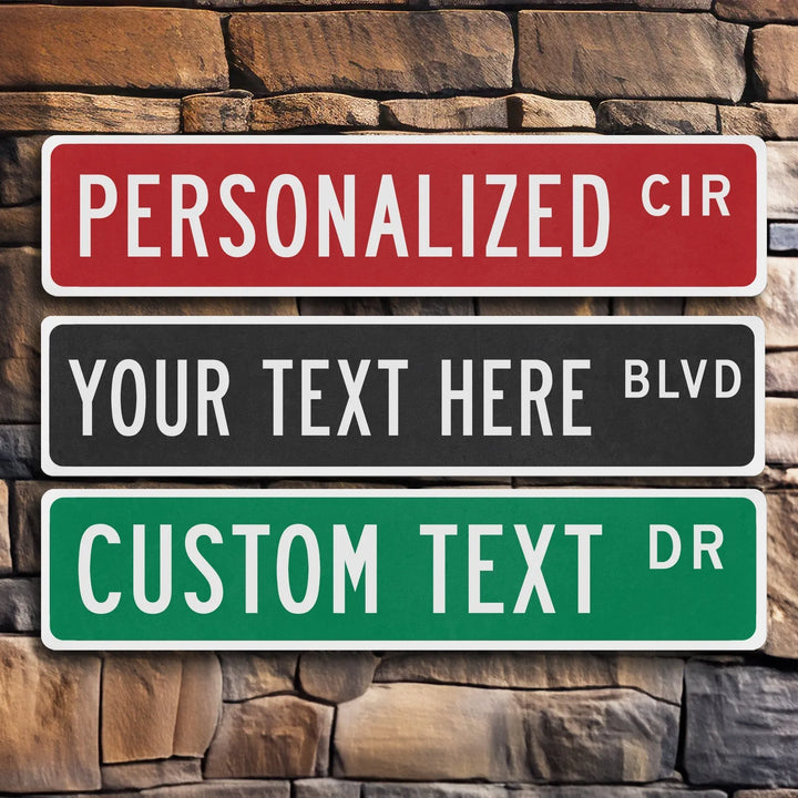 Three rectangular metal street signs with customizable text, mounted on a stone wall background