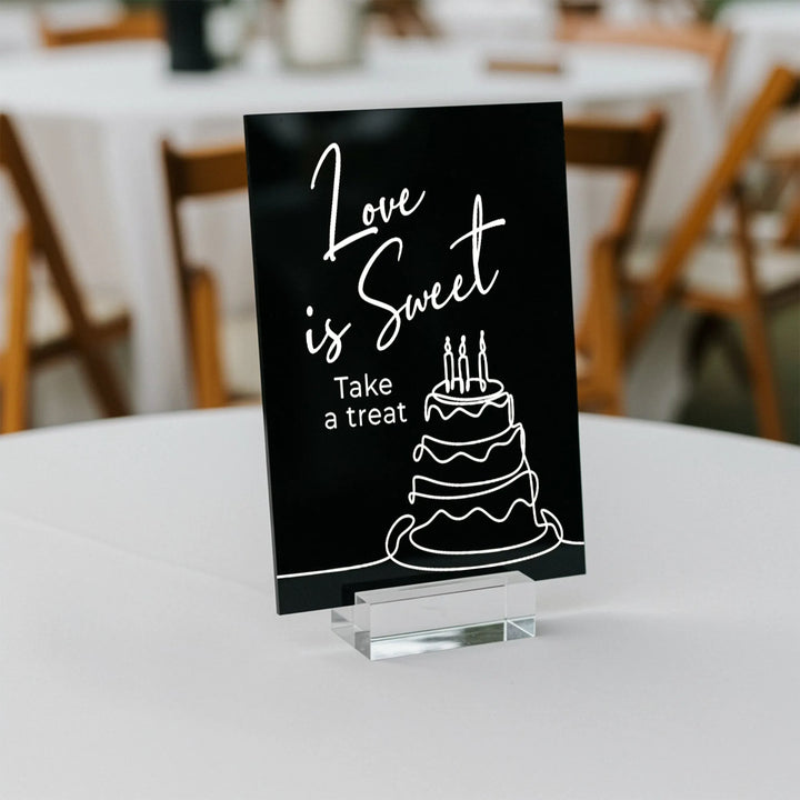 Black acrylic wedding table sign with white text 'Love is Sweet Take a treat' and cake illustration