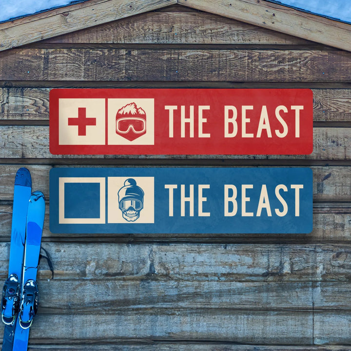 Two metal ski trail signs reading 'The Beast' with ski and mountain icons, mounted on wooden wall with blue skis