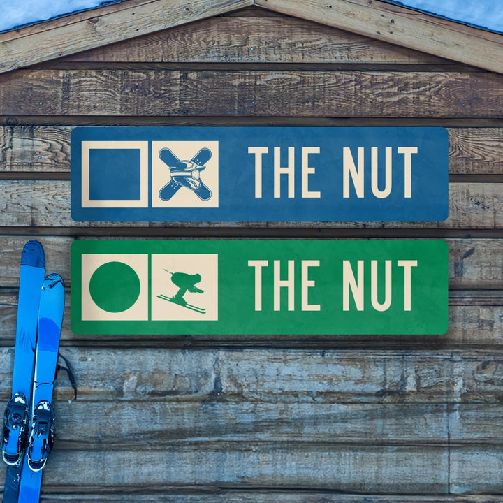 Metal ski trail signs on wooden wall labeled The Nut with ski icons and blue skis leaning against it