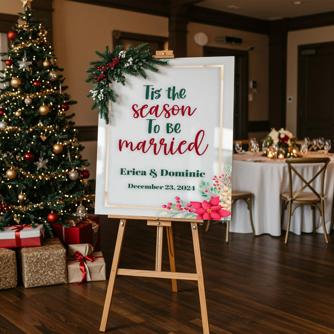 Christmas-themed wedding welcome sign with greenery and poinsettias, decorated tree, and wrapped gifts