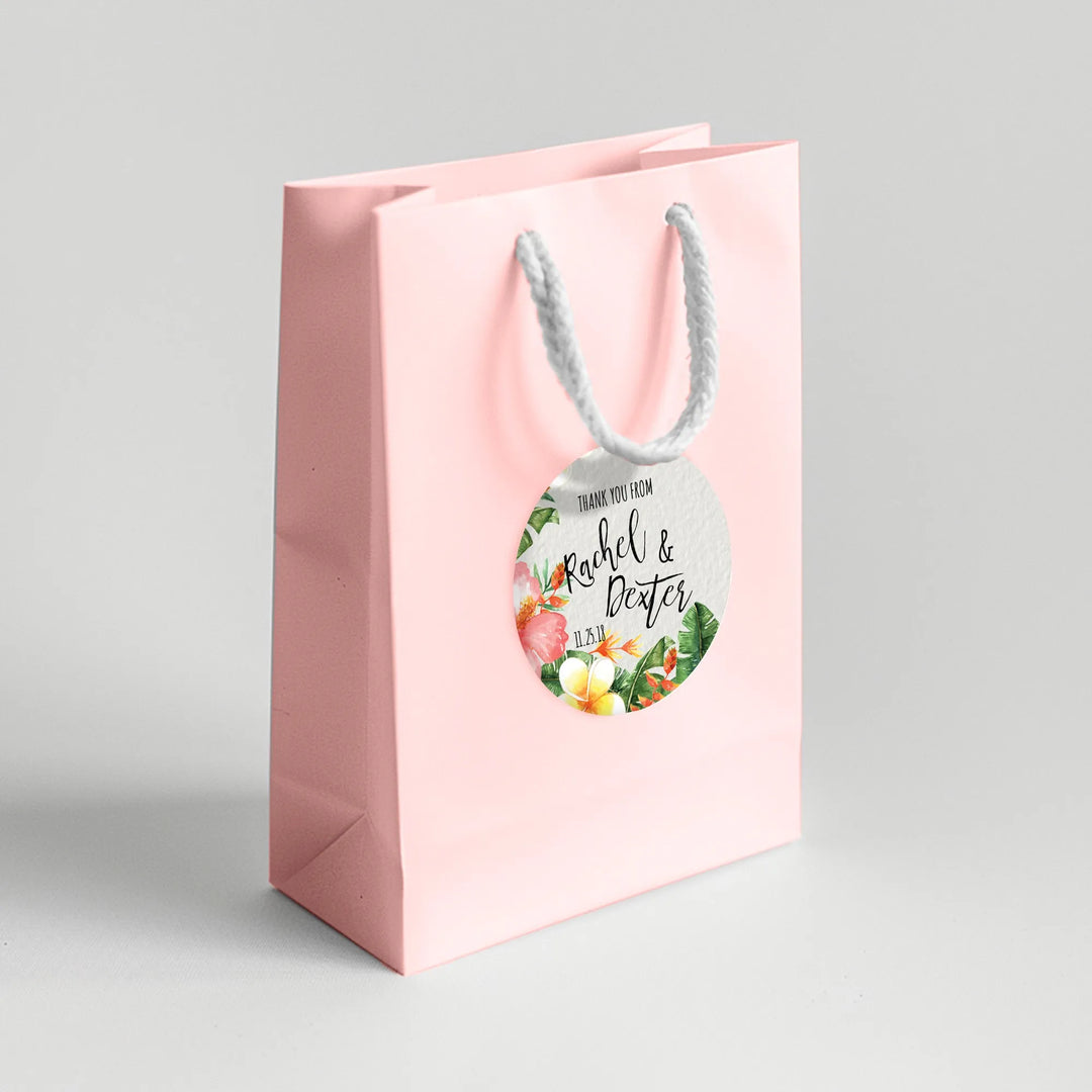Pink gift bag with tropical floral wedding favor label and white rope handle.