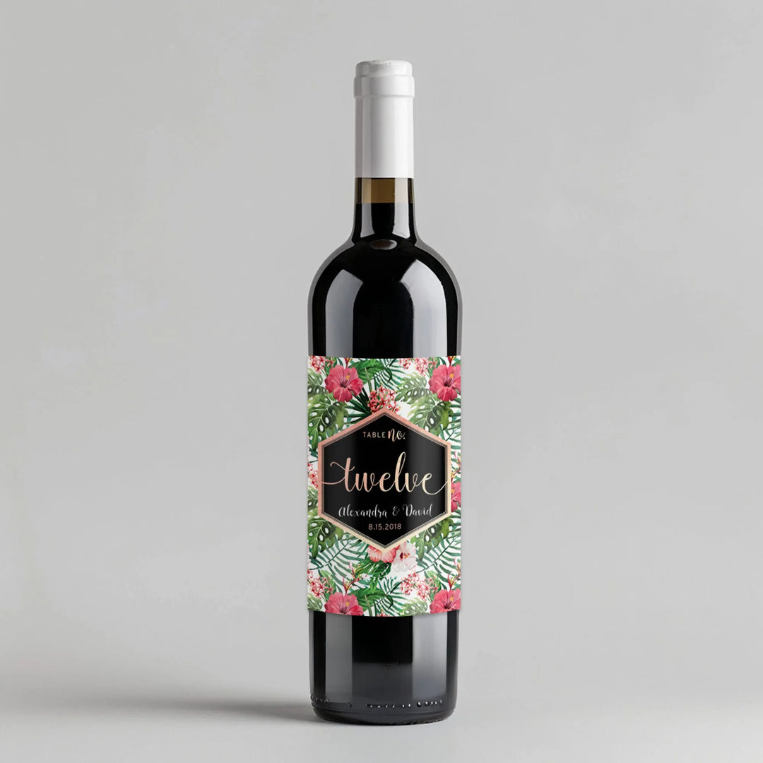 Wine bottle with tropical rose gold floral table number label on gray background