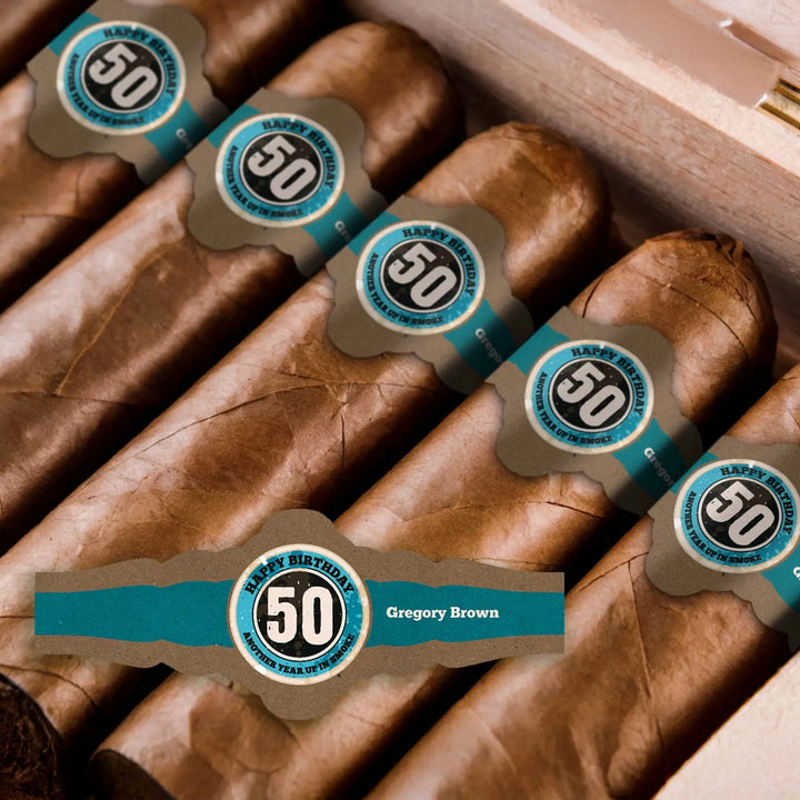 Close-up of custom 50th birthday cigar bands with blue and silver design in a cigar box.