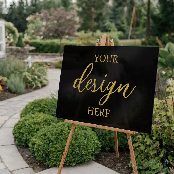 Customizable black acrylic sign with gold text on wooden easel in garden setting