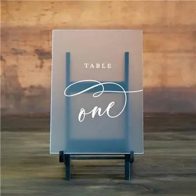 Acrylic table number sign with elegant script reading 'Table one' on wooden surface