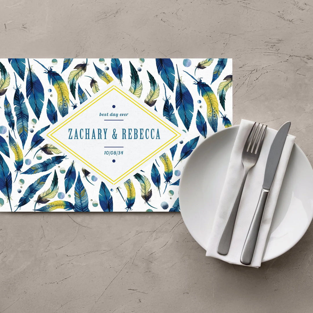 Watercolor feather placemat with custom names, next to plate with napkin, fork, and knife.