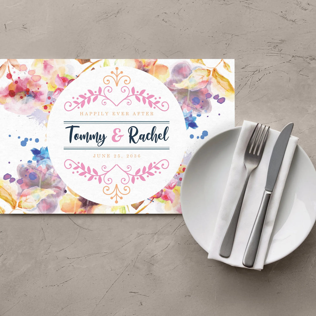 Watercolor floral wedding placemat with plate, fork, knife, and napkin on gray table.