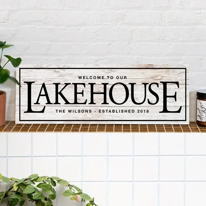 Rustic wood welcome to our lake house sign on tile shelf, farmhouse decor with plants