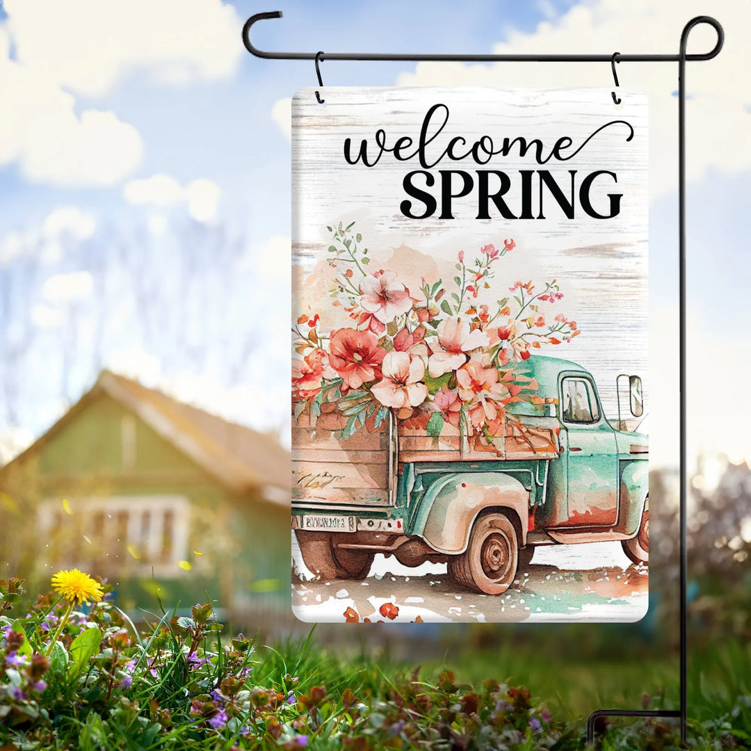 Welcome spring garden flag with vintage turquoise truck carrying pink flowers in bright outdoor setting