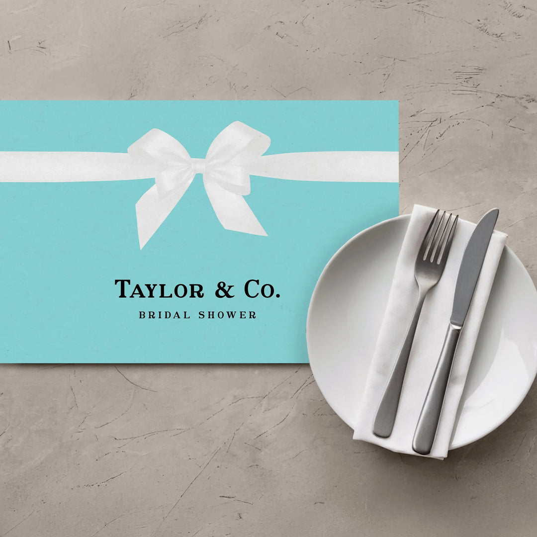 Blue bridal shower placemat with white bow, plate, napkin, and cutlery on table
