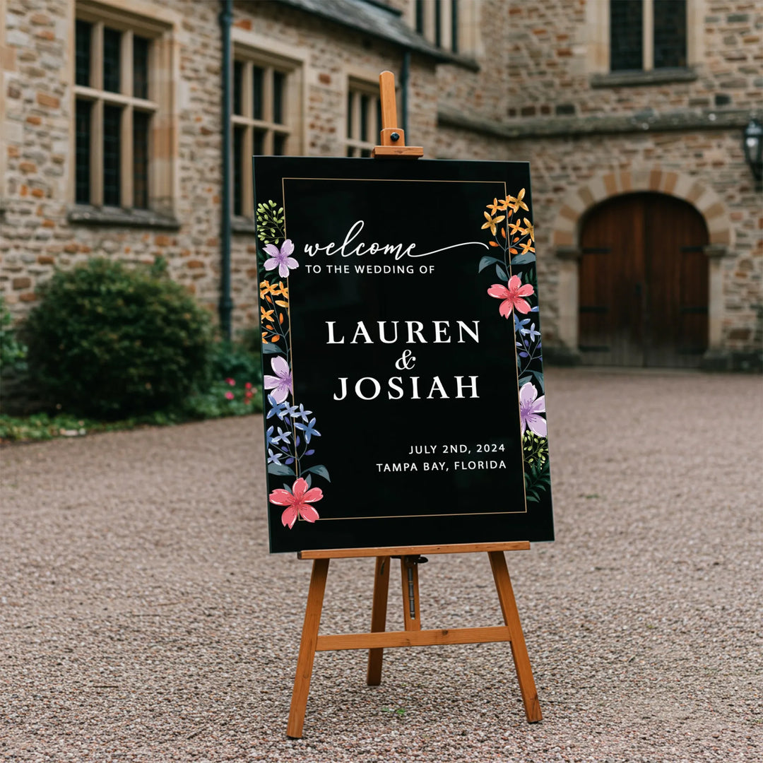 Elegant black wedding welcome sign with colorful wildflowers on wooden easel in courtyard