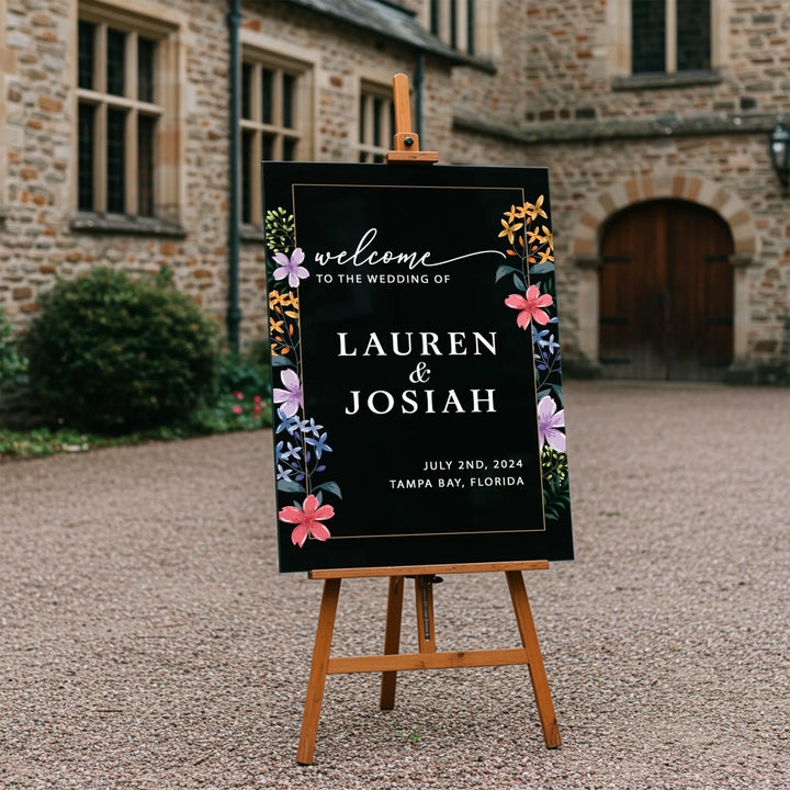 Elegant black wedding welcome sign with colorful wildflowers on wooden easel in courtyard